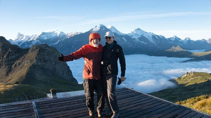 Two men standing on a roof with mountains in the background

Description automatically generated