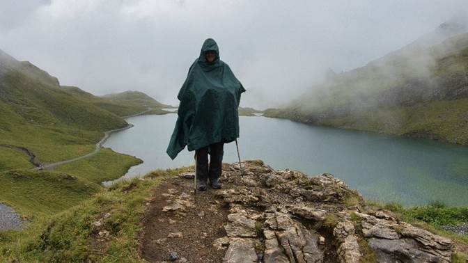 A person standing on a rock with a rain poncho

Description automatically generated