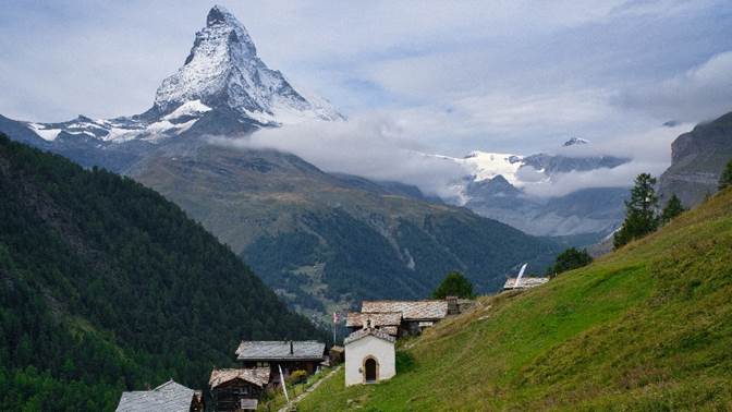 A small village in a valley with mountains in the background

Description automatically generated