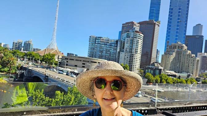 A person wearing sunglasses and a hat with a city in the background

Description automatically generated